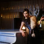 Woman in a vintage burlesque-style dress holding a drink beside a piano inside 1923 Prohibition Bar, one of the best bourbon bar and event space in Las Vegas.