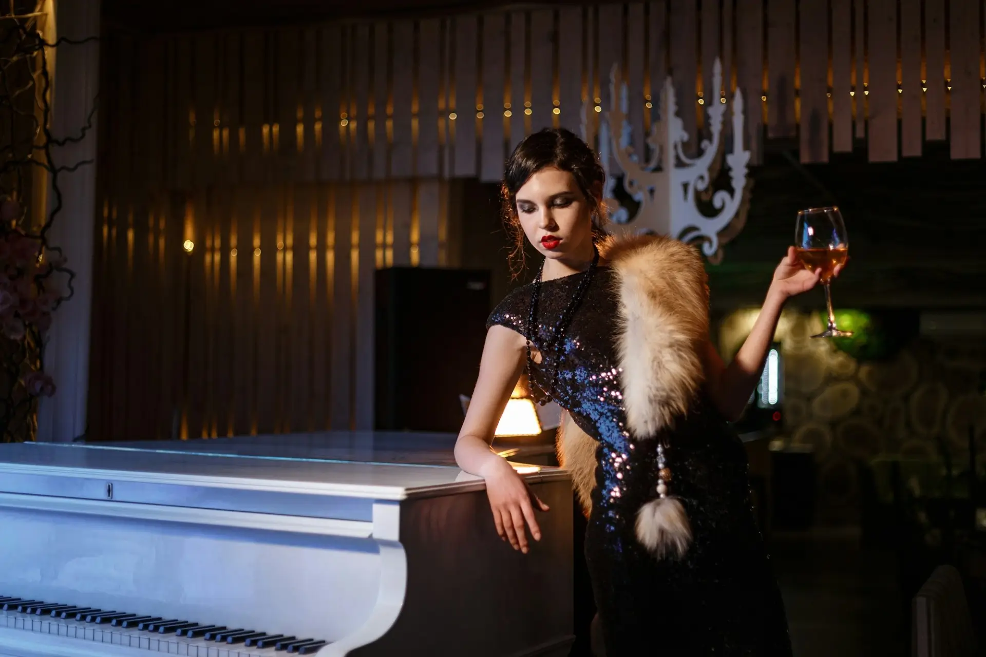 Woman in a vintage burlesque-style dress holding a drink beside a piano inside 1923 Prohibition Bar, one of the best bourbon bar and event space in Las Vegas.