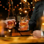 Two guests toasting with glasses of premium bourbon on the rocks inside 1923 Prohibition Bar, a hidden speakeasy bar located in Las Vegas.